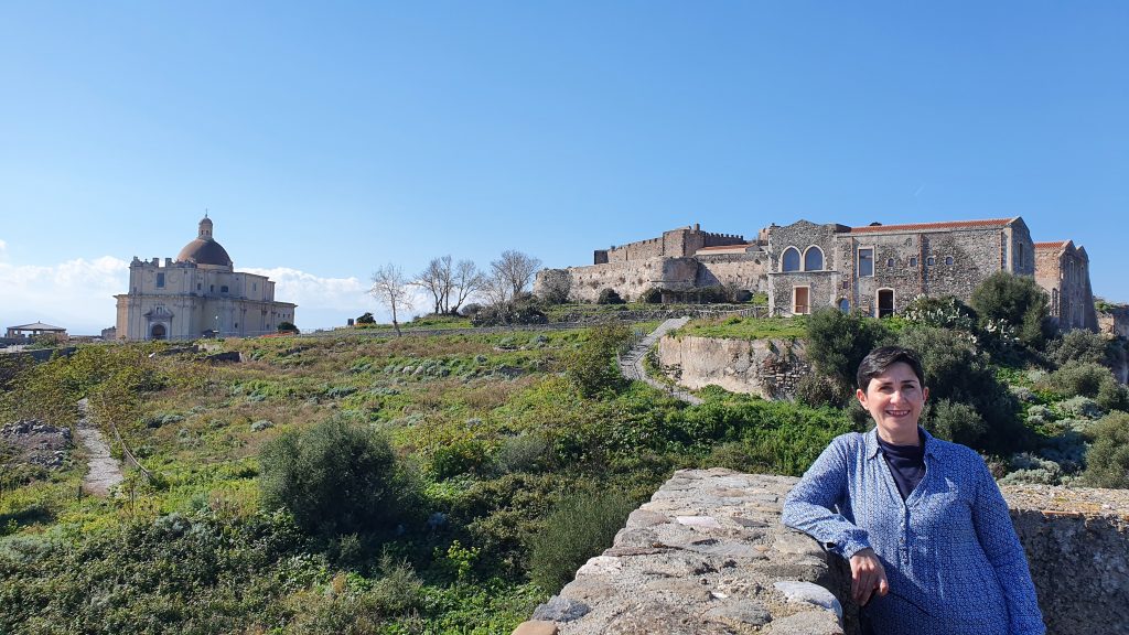 Guida turistica e sullo sfondo il Castello di Milazzo